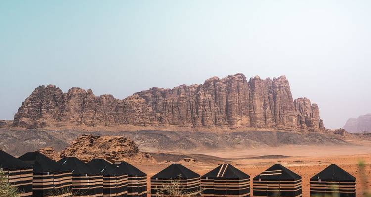 Reihe traditioneller Beduinenzelte mit dramatischen Sandsteinfelsen des Wadi Rum im Hintergrund