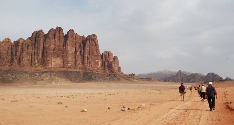 Los senderistas cruzan la inmensa llanura desértica de arena roja bajo formaciones rocosas imponentes en Wadi Rum.