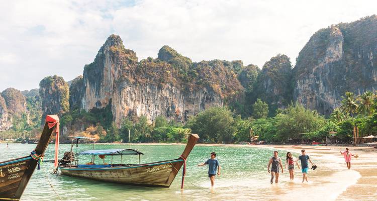 Des bateaux à longue queue flottent sur une eau émeraude près de falaises calcaires imposantes à Railay Beach, Krabi.