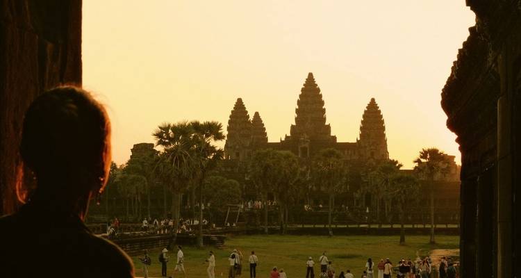 Silhouetted against a golden sunrise, Angkor Wat’s iconic towers rise above visitors exploring the grounds.