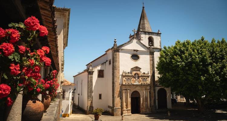 Petite église historique avec clocher dans une rue de village portugais ensoleillée bordée de fleurs rouges