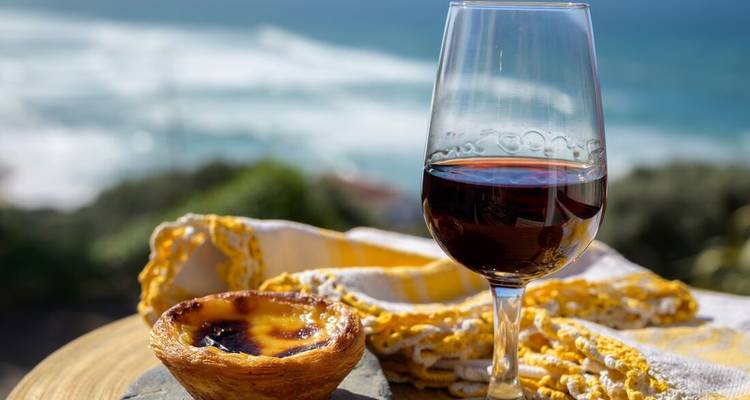 Verre de vin rouge et pastel de nata surplombant un littoral atlantique bleu