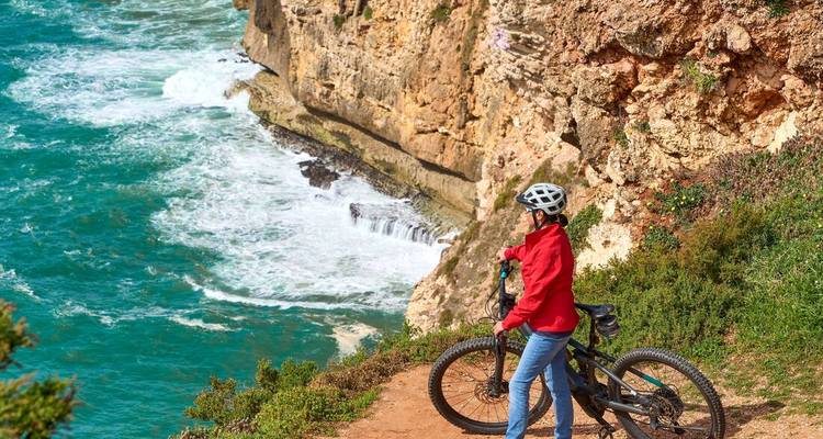 Cycliste en veste rouge en pause au bord de la falaise surplombant les vagues qui s'écrasent loin en dessous