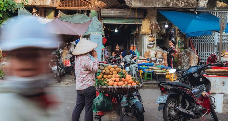 Un étal de marché vietnamien animé vend des fruits frais tandis que les scooters se faufilent