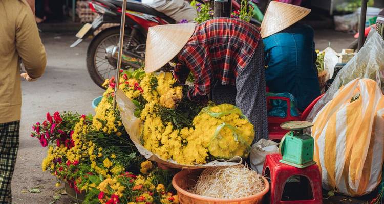 Des bouquets colorés et des paniers de fleurs exposés sur un marché de rue avec des vendeurs portant des chapeaux coniques