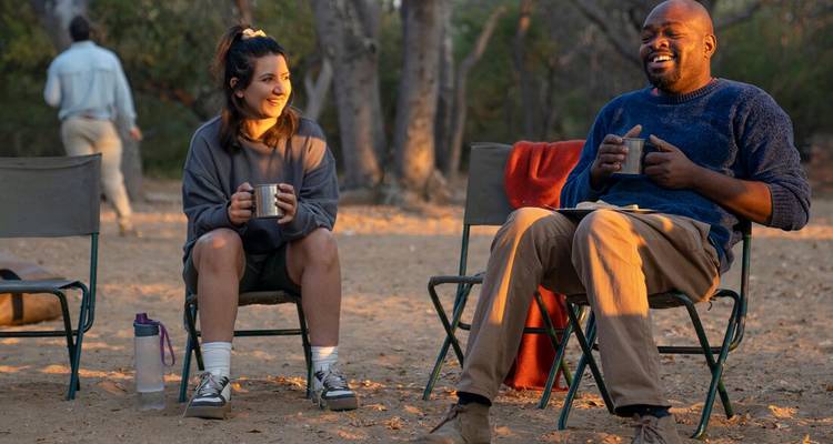 Viajeros relajándose con bebidas calientes en sillas de camping en el monte al atardecer.