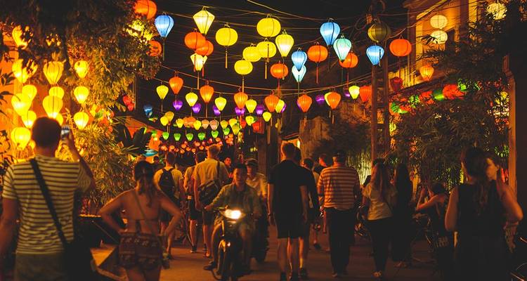 Crowds wander through Hoi An’s lantern-lit streets glowing with multicolored lights at night.