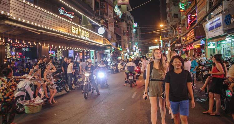 Bustling nightlife scene on Bui Vien street with neon signs, motorbikes and pedestrians.