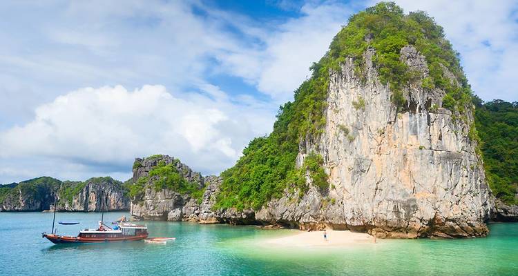 Turquoise bay with towering limestone karst and small sandy beach visited by a boat.