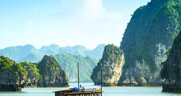 Un barco junco de madera tradicional navega entre los espectaculares karsts de piedra caliza de la Bahía de Halong bajo un cielo brillante.