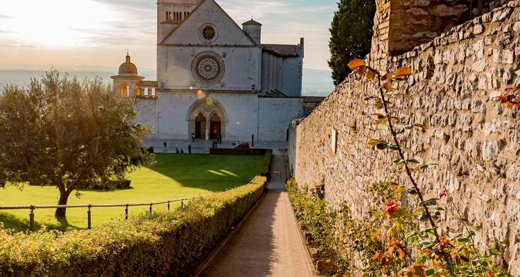 Una basílica de piedra iluminada por el sol domina césped bien cuidado y un sendero bordeado de flores.