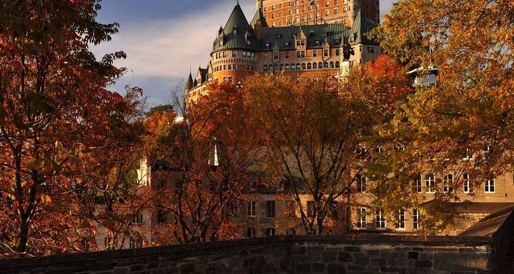 Château Frontenac rodeado de follaje otoñal vibrante bajo un cielo azul.
