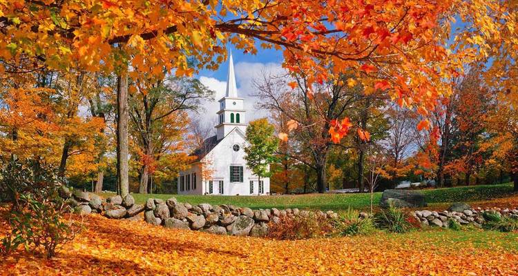 Charmante église blanche de Nouvelle-Angleterre avec haut clocher entourée de feuillage automnal orange vibrant et tapis de feuilles