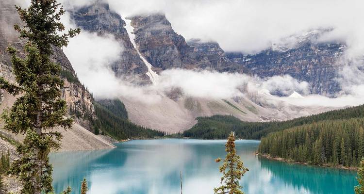 Turquoise alpenmeer gespiegeld door torenhoge rotspieken gehuld in wervelende wolken
