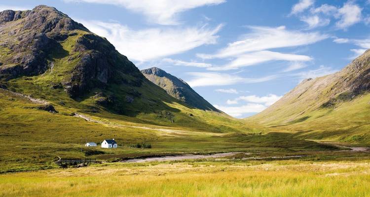 Ein kleines weißes Haus in einem grünen Tal, umgeben von Bergen.