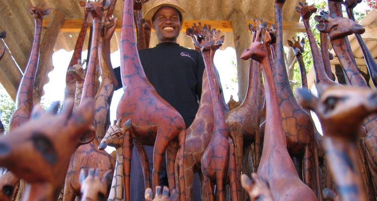 Homme souriant parmi des sculptures de girafes en bois sur un marché.