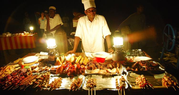 Vendeur de nourriture de rue avec une variété d'aliments grillés sur une table.