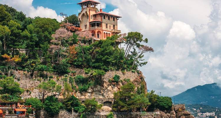 Villa pintoresca encaramada en un acantilado rocoso mediterráneo rodeada de vegetación exuberante y terrazas de piedra.