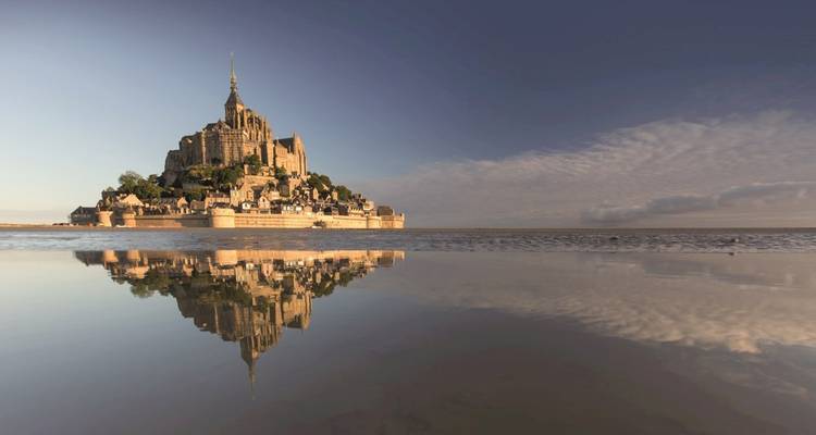 Mont Saint-Michel se reflétant dans l'eau sous un vaste ciel à marée basse.