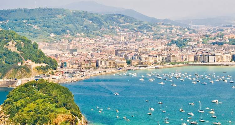 Panoramastadtbild der Küste von San Sebastián mit türkisfarbener Bucht, die von weißen Booten gesäumt ist.