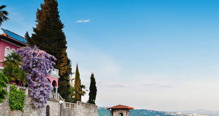 Élégante villa côtière drapée de fleurs violettes surplombant un rivage adriatique paisible.