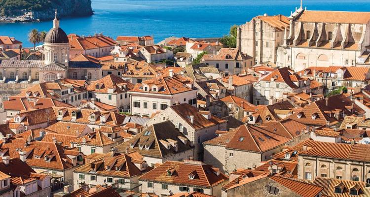 Terracotta rooftops of Dubrovnik’s Old Town hug the Adriatic coast beneath a clear sky.
