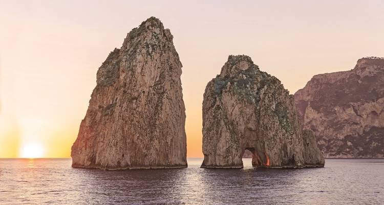 Formaciones rocosas de Faraglioni en medio de una puesta de sol sobre el mar cerca de Capri.