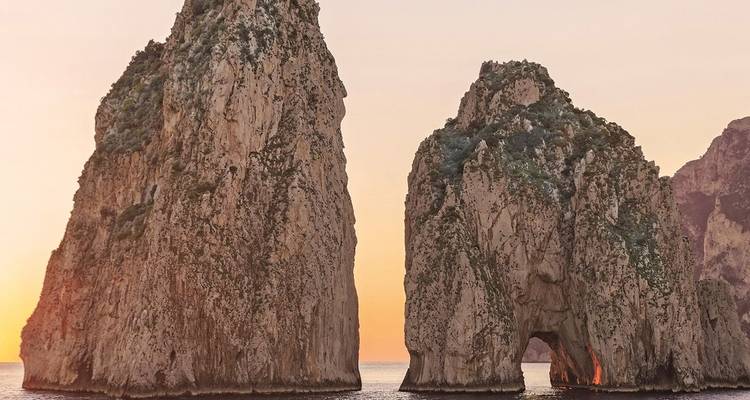 Lueur du coucher de soleil derrière les imposants rochers Faraglioni s'élevant des eaux turquoise au large de Capri.