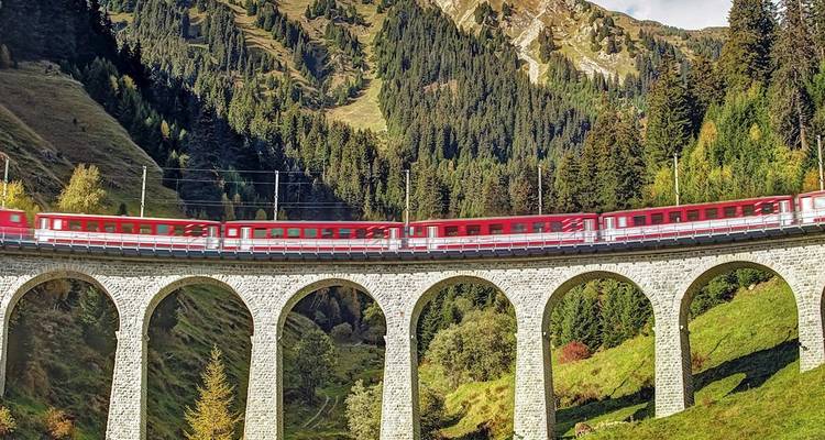 Roter Panoramazug, der ein hohes steinernes Viadukt in den üppigen Schweizer Alpen überquert