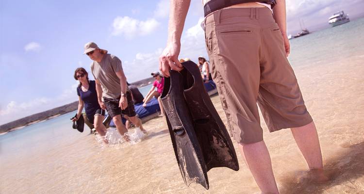 Reizigers waden van een opblaasbare boot naar het strand en dragen snorkelvinnen in ondiep turquoise water.