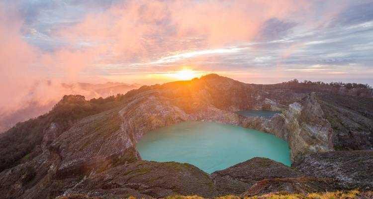 Sunrise light illuminating vibrant turquoise crater lakes within a rugged volcanic caldera