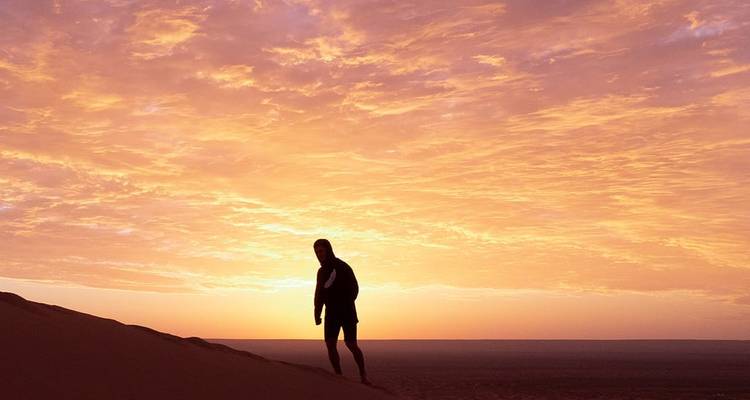 Persoon die bij zonsondergang over een zandduin loopt