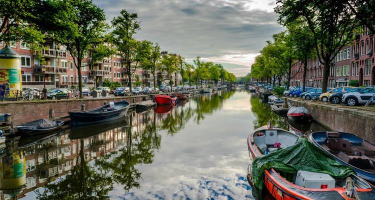 Pintoresco canal bordeado de barcos y árboles que se reflejan en el agua.