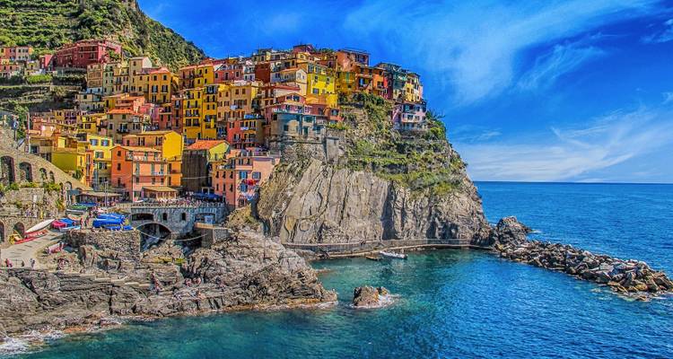 Colorful cliffside village of Manarola overlooking emerald waters and rocky coastline in bright sunshine.