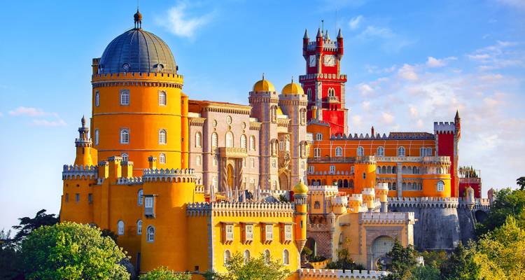 Fairytale-like Pena Palace in Sintra with vivid yellow and red towers perched atop a lush forested hill.
