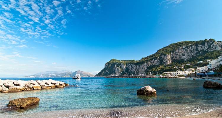 Crystal-clear turquoise water and rugged cliffs of Capri with a boat anchored offshore under a bright sky.