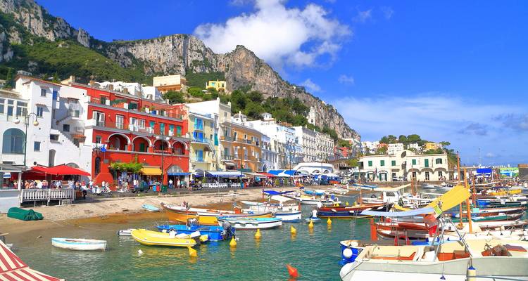 Bustling Capri harbour with colourful buildings and numerous boats moored along the clear water.