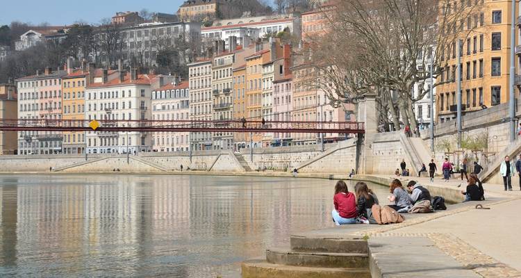 Des gens se détendent sur une promenade au bord de la rivière devant des bâtiments colorés.