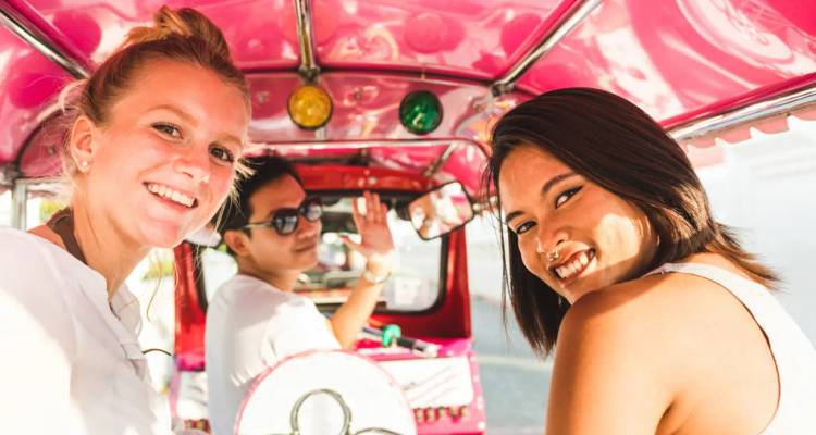 Des voyageurs souriants dans un tuk-tuk rose vif, faisant signe à la caméra.