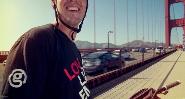 Ein Radfahrer lacht während der Fahrt über die Golden Gate Bridge an einem sonnigen Nachmittag.