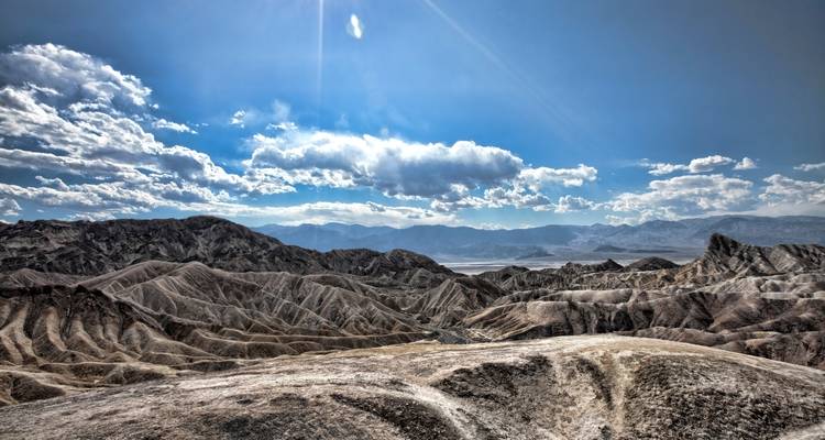 Weitläufige Aussicht über die rauen, sonnengebleichten Grate und Salzseen des Death Valley unter einem strahlend blauen Himmel.
