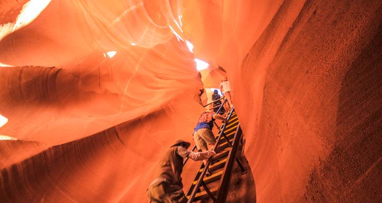 Les voyageurs montent une échelle en bois à l'intérieur des murs orange lumineux d'un canyon étroit.