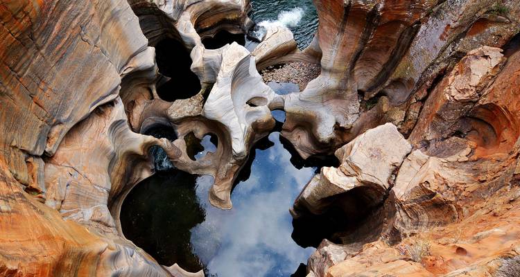 Top-down view of sculpted sandstone potholes with dark reflective pools.