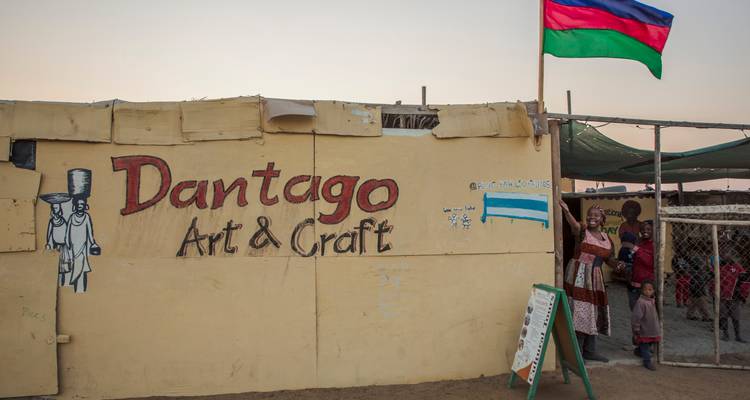 Small roadside craft shop with painted sign and Namibian flag fluttering at dusk.