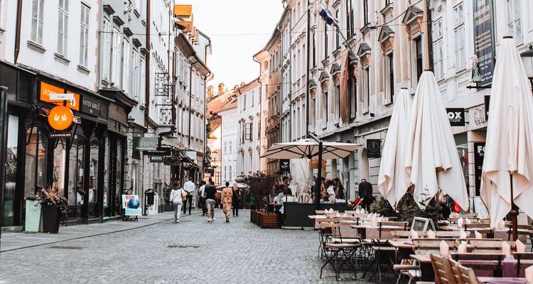 Pedestrians stroll along a charming cobblestone street lined with cafes and historic facades in Ljubljana’s old town.