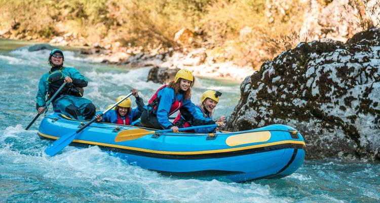 A family paddles a blue inflatable raft through lively whitewater on the emerald Soča River.