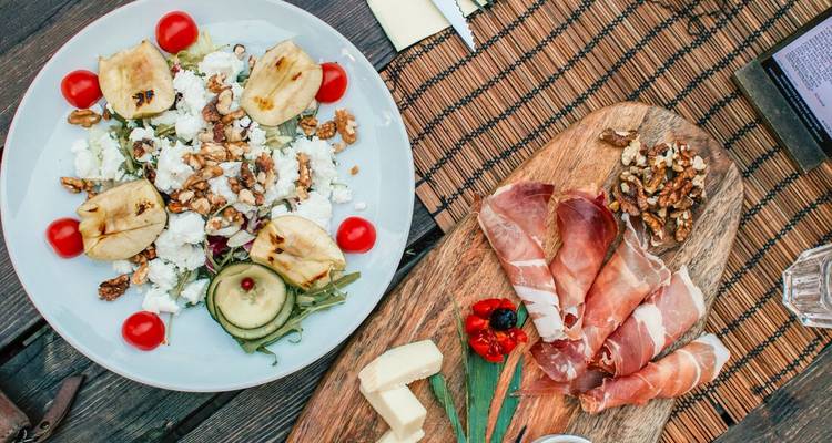 Rustic wooden table set with a fresh Slovenian platter of salad, prosciutto, walnuts and cheese.