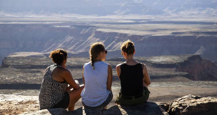 Tres personas sentadas en el borde de un cañón disfrutando de la vista.
