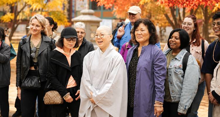 Groupe de visiteurs internationaux posant avec une religieuse bouddhiste dans un temple pendant la saison des feuillages automnaux