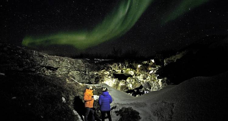 Dos personas observando la Aurora Boreal en un entorno nevado.